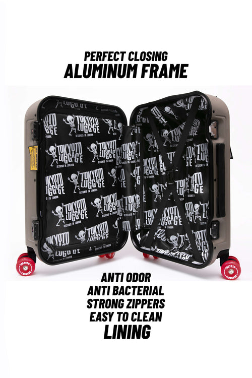 A hard-shell suitcase shown open on a white background, with black text above and below describing features such as an aluminum frame, anti odor, anti bacterial, strong zippers, and easy-to-clean lining. The inside of the suitcase has a black background with a repeating white Tokyo Drift logo pattern, and the exterior appears dark gray or black with red wheels.
