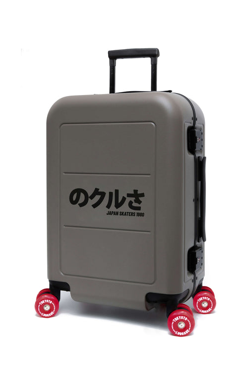 A gray hard-shell suitcase with a black telescoping handle and four red wheels, featuring the Japanese text 'のアル JAPAN SAILERS 1980' printed on the front.