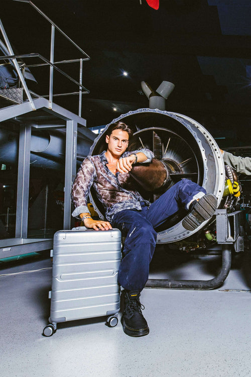 Man sitting on a Aluminum  suitcase in front of a large fan in an industrial setting