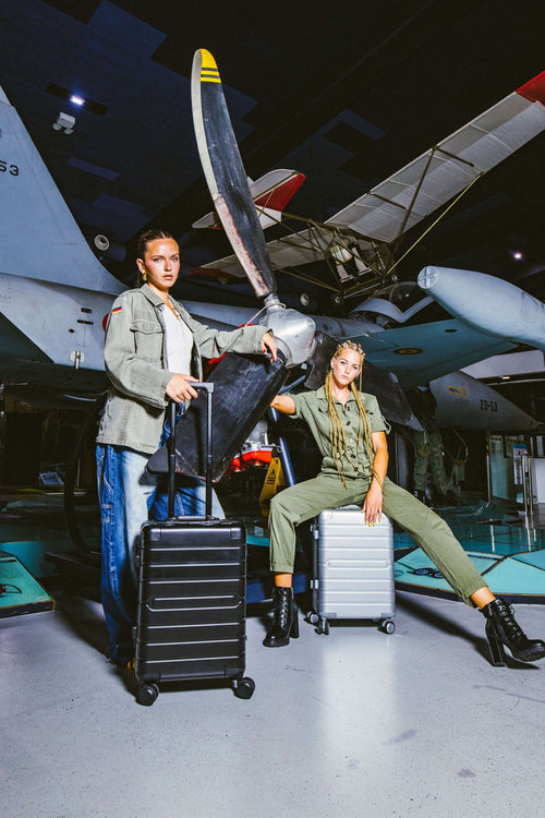 Two people in military-style outfits with 2 aluminium suitcases with aircraft in the background.