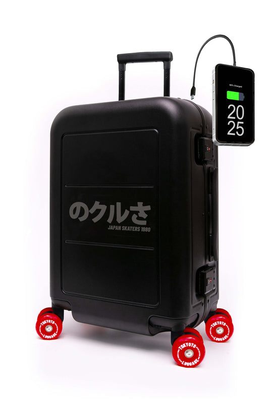 A black hard-shell suitcase with red skate wheels and a built-in power bank, shown on a white background. The suitcase features the text 'のベンイズ JAPAN SEATERS' in white.