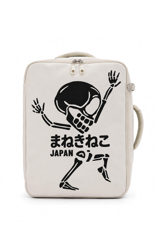 An off-white canvas backpack featuring a black graphic of a dancing skeleton with Japanese text and 'JAPAN' printed below it, set against a plain white background.