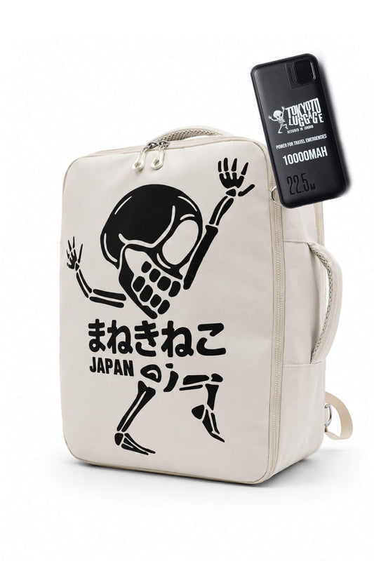 An off-white canvas backpack featuring a black graphic of a dancing skeleton with Japanese text and 'JAPAN' printed below. A black phone case with 'TRICK OR TREAT' and '1000MAH' branding is attached to the side of the bag.